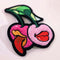 Patch featuring two cherries with expressive lips, one with a tongue sticking out, set against a white background. The design is playful and vibrant, combining bold colors with a fun, cheeky style.